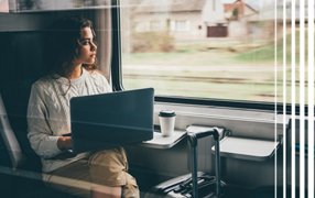 Woman on train with laptop looking out window